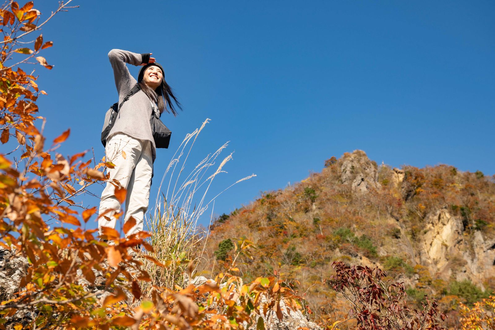 男体山周辺の岩場から紅葉の山並みを望むハイカー